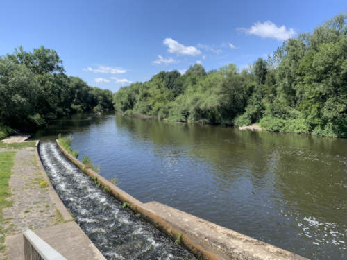 Der Fluss Lahn hier in Gießen mit einer Bootsrutsche. Links und rechts befinden sich Bäume an einem leicht bewölkten Himmel.