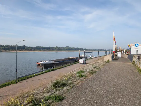 Zevenaar Tolkamer mit einer kleinen Fußgängerzone und Rheinschiffe auf dem Rhein an einem sonnigen Tag. 

In der Fußgängerzone befinden sich einige Lokale, wo beim Fahrrad absteigen muss.