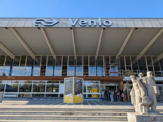 Venlo Bahnhof Station Eingang mit Figuren aus Stein. Unter dem Bahnhofsdach steht der Hinweis mit Einschränkungen im Bahnverkehr für Ende Oktober 2026 in den Niederlanden
